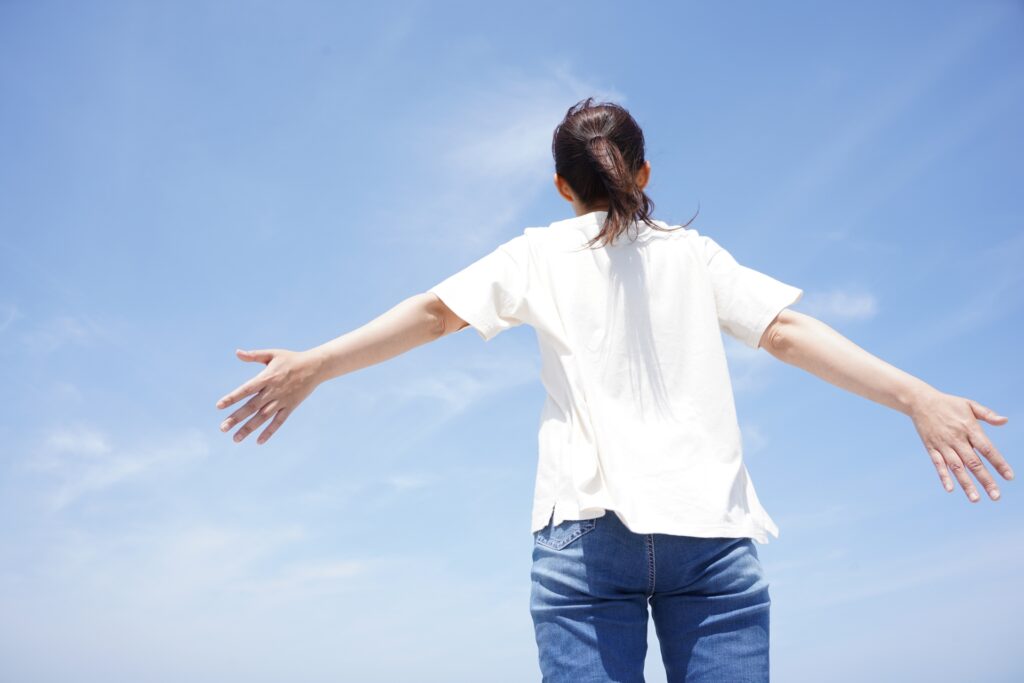屋外で両手を広げてリラックスしている女性の後ろ姿