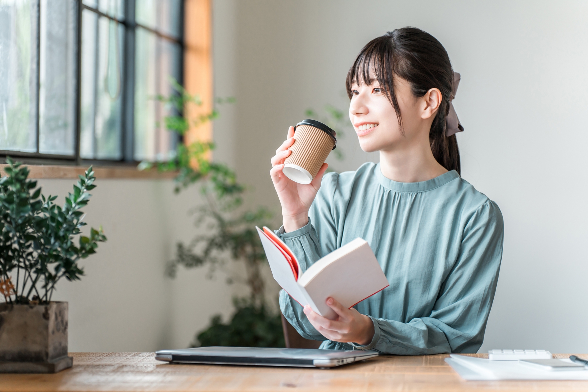 窓辺でコーヒーを飲みながら、ゆったりと読書を楽しんでいる女性。